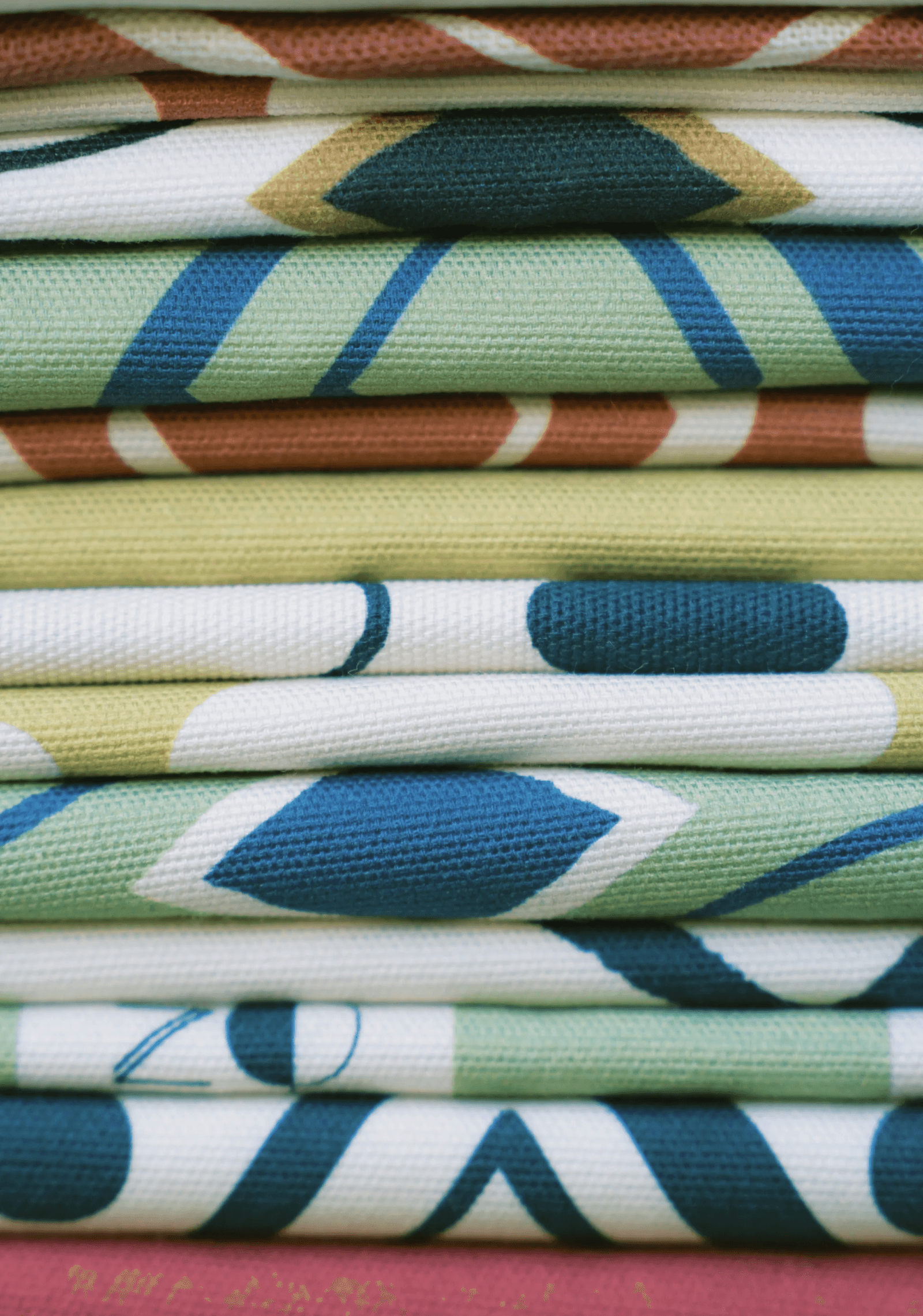 Stack of folded KIND textiles in blue, green and terracotta